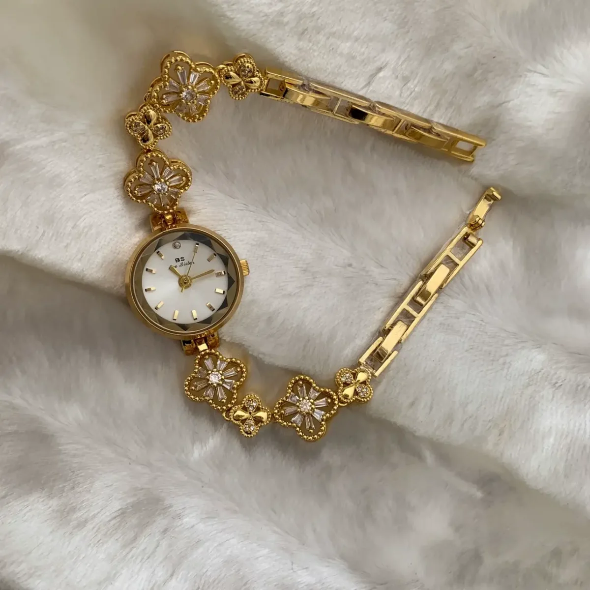 Top-down view of a vintage gold watch with a diamond-studded clover link bracelet, resting on a white, soft fabric background. Features the BS Bee Sister brand.