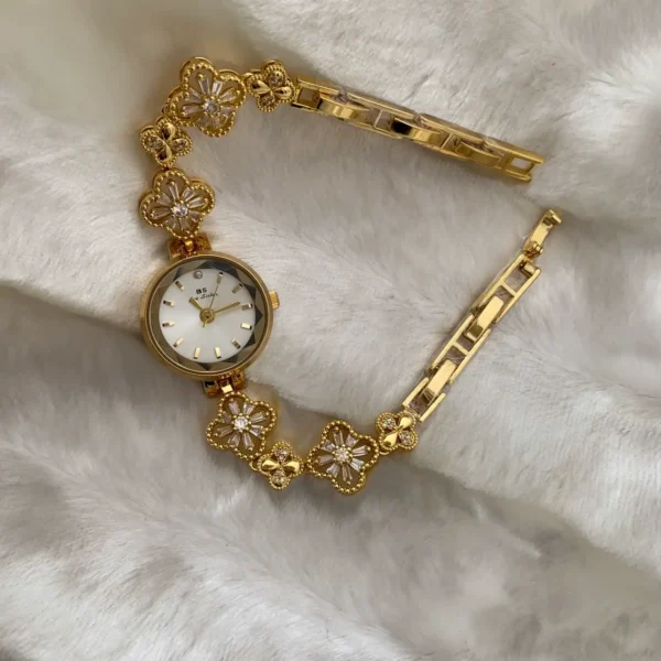 Top-down view of a vintage gold watch with a diamond-studded clover link bracelet, resting on a white, soft fabric background. Features the BS Bee Sister brand.