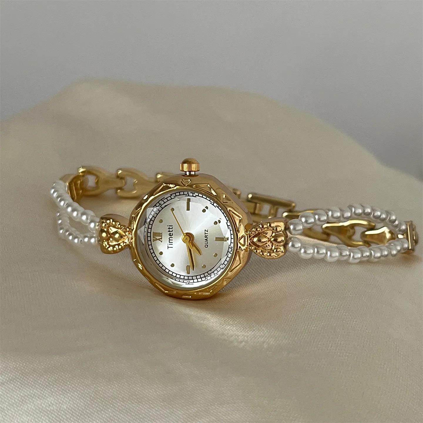 Vintage gold watch with a double-strand pearl bracelet and delicate gold link chain, showcasing the Timetti quartz dial on a soft silk background.