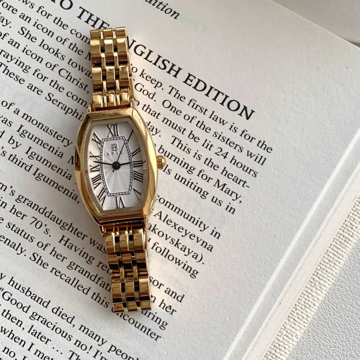 Close-up of vintage gold women’s tonneau watch with Roman numeral dial on book