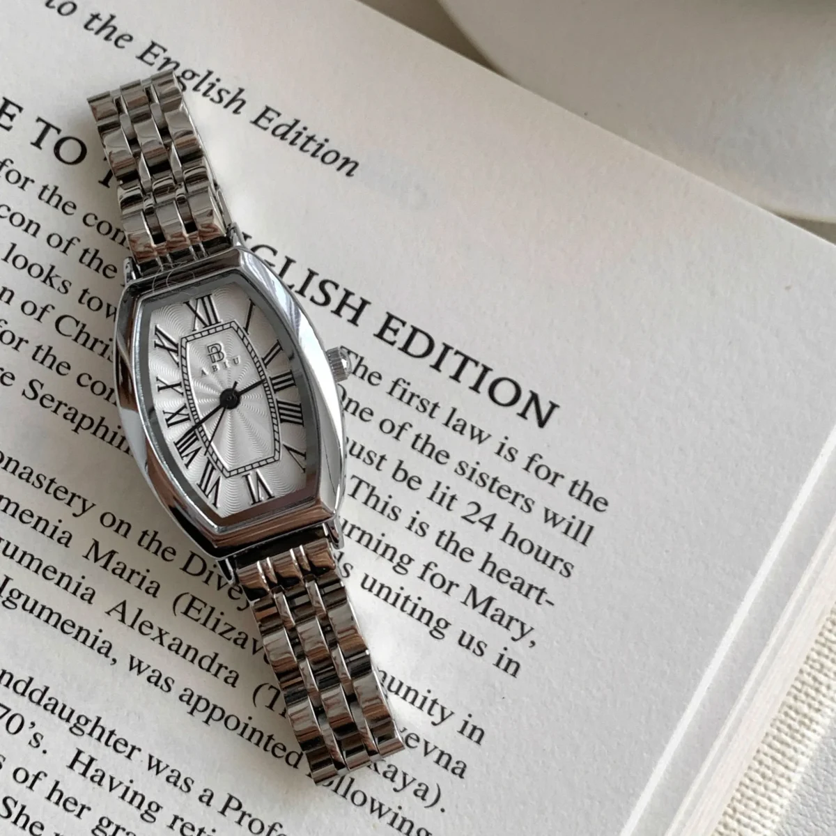 Close-up of vintage silver women’s tonneau watch on book with Roman numerals