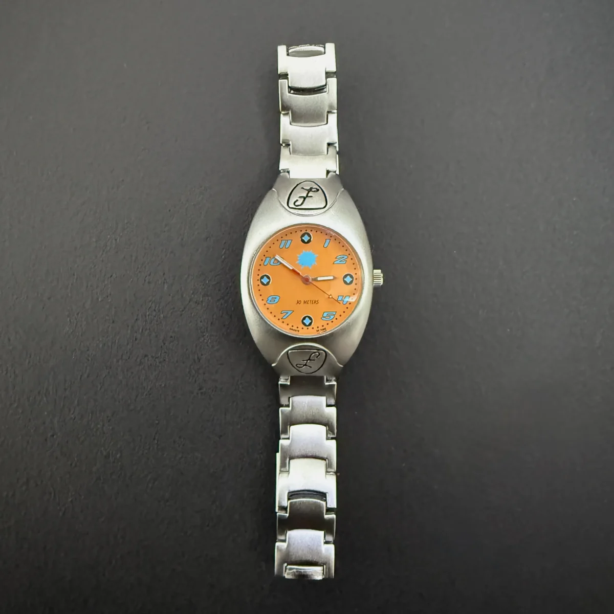 Vintage silver women’s quartz watch with orange dial and sunburst spark design