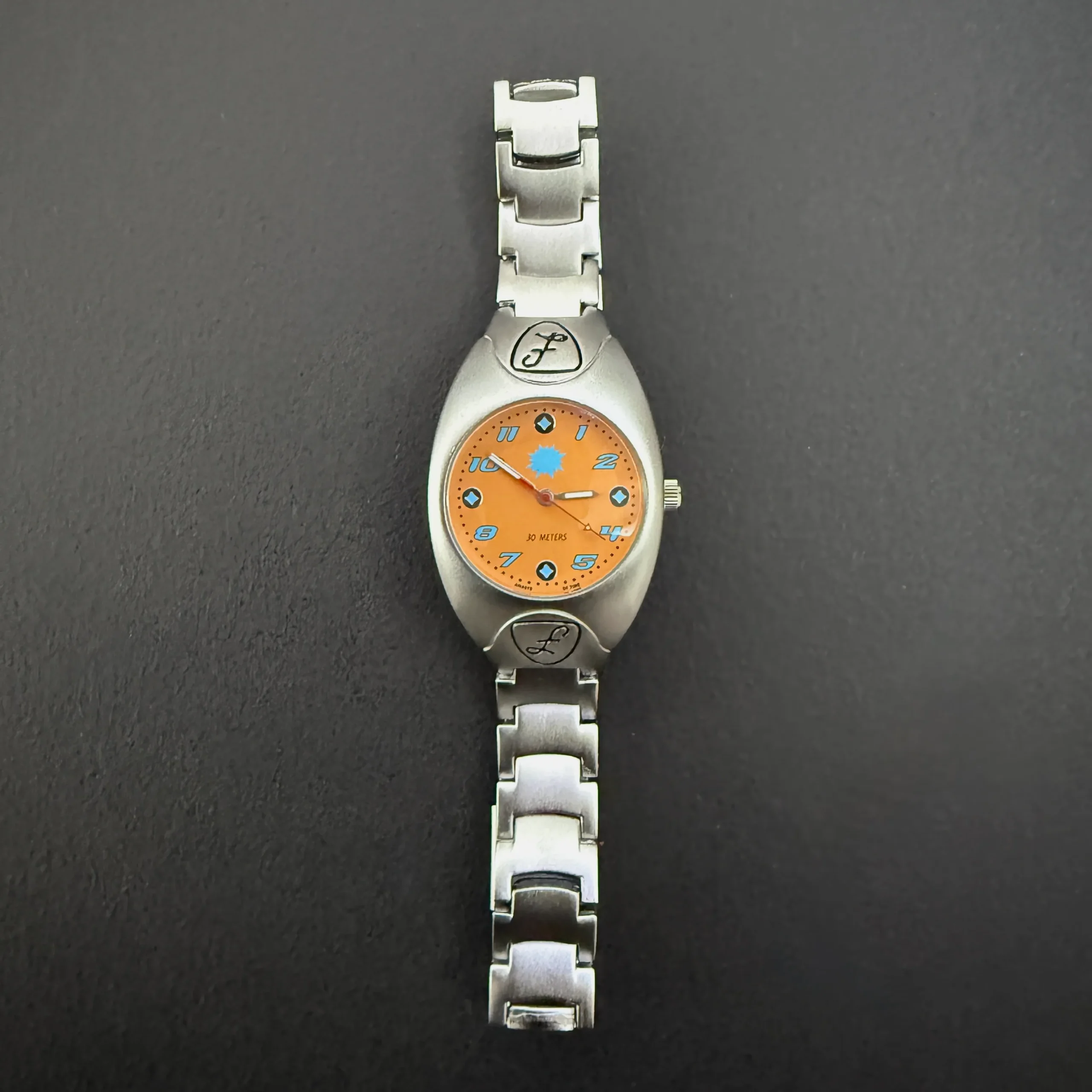 Vintage silver women’s quartz watch with orange dial and sunburst spark design