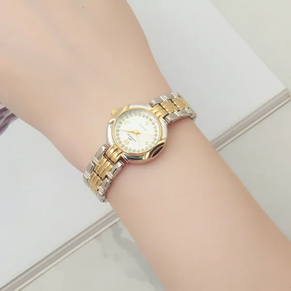 Wrist shot of a vintage women's gold quartz watch with a white dial and traditional Arabic numeral markings.